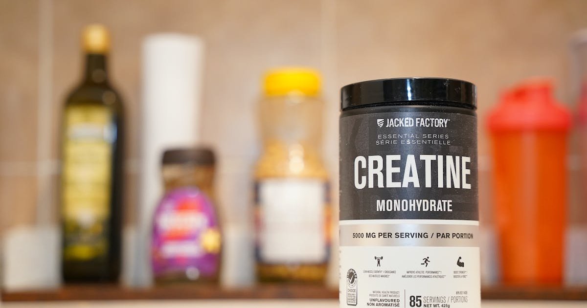 Woman holding a scoop of creatine powder next to a glass of water on a kitchen counter